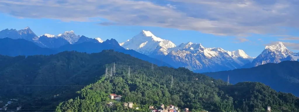 Kanchenjunga mountain range, covered with snow, with lush green hills under a clear blue sky in Sikkim